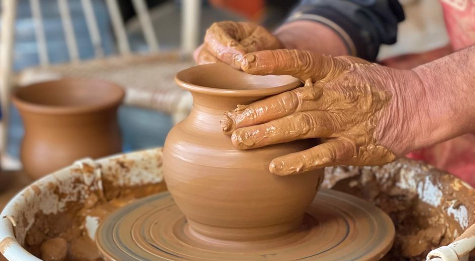 Hands pulling the wall of a pot on the wheel